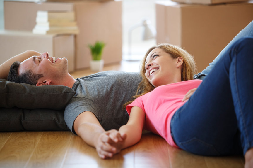 Smiling couple laying on floor with moving boxes in background.